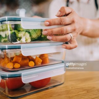 Close-up shot of female hands holding glass containers with fresh raw vegetables.
